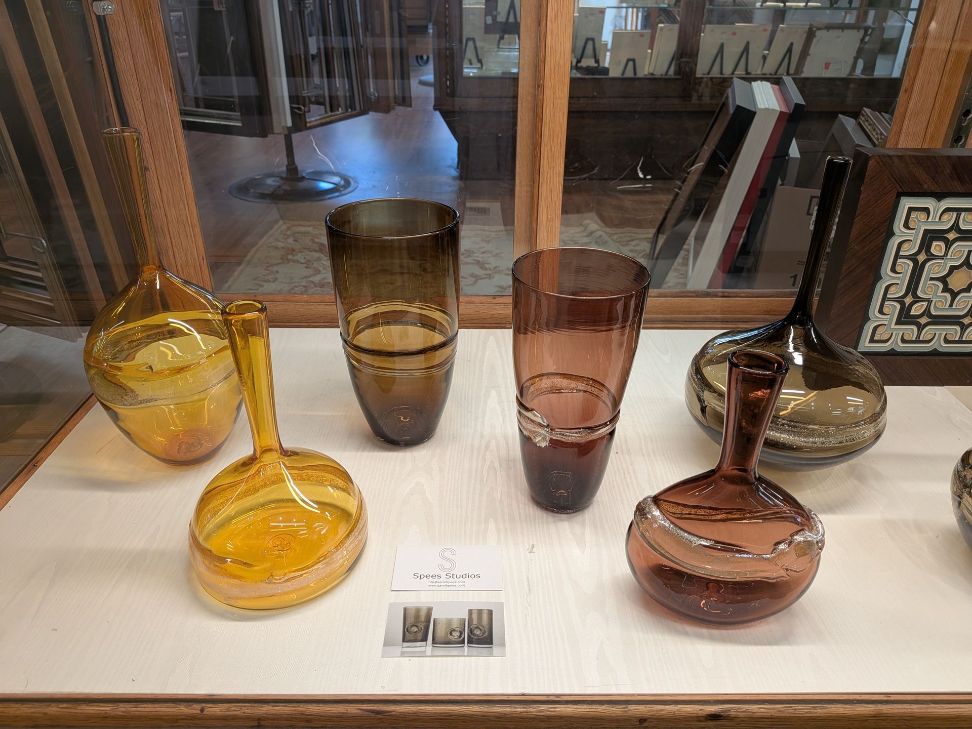 Display of colorful glass vases and bowls on a white shelf in a store or gallery.