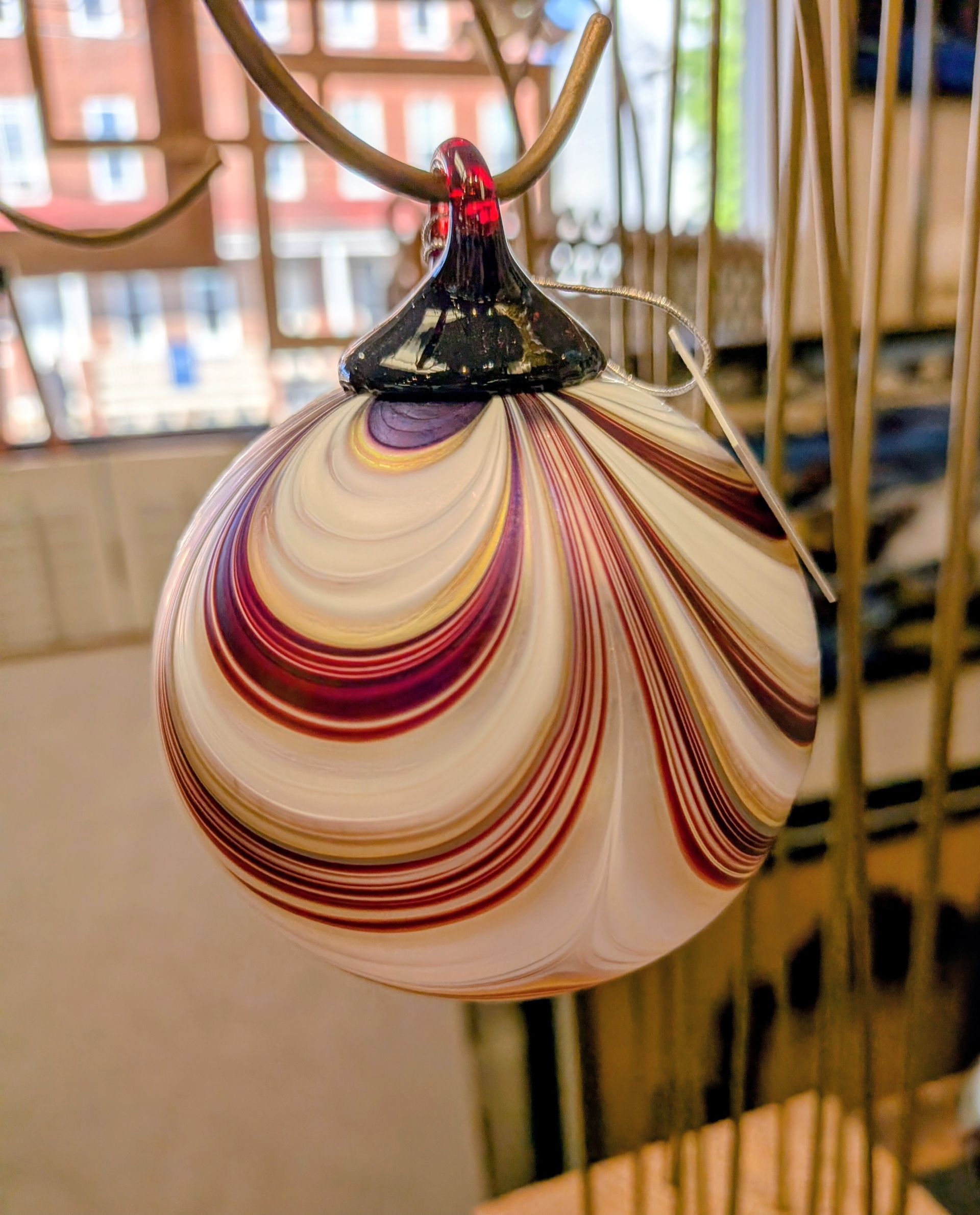 White teardrop glass ornament with maroon and gold swirls hanging indoors.