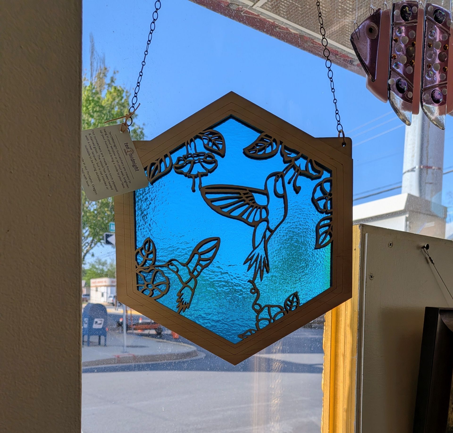 Hexagonal stained-glass bee decoration with blue background hanging in a sunlit window.