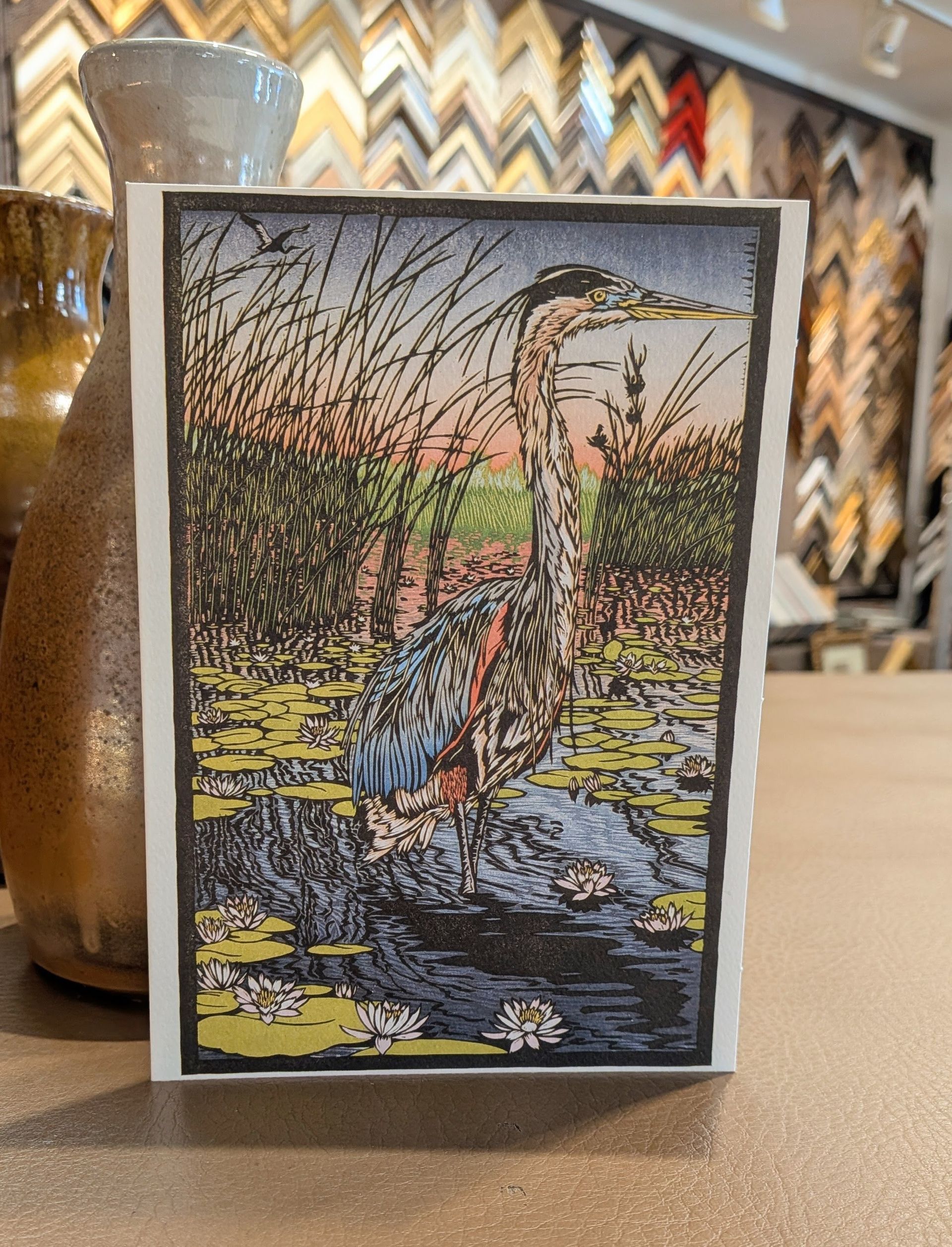 Heron standing in marsh grass with water, framed as a small decorative artwork.