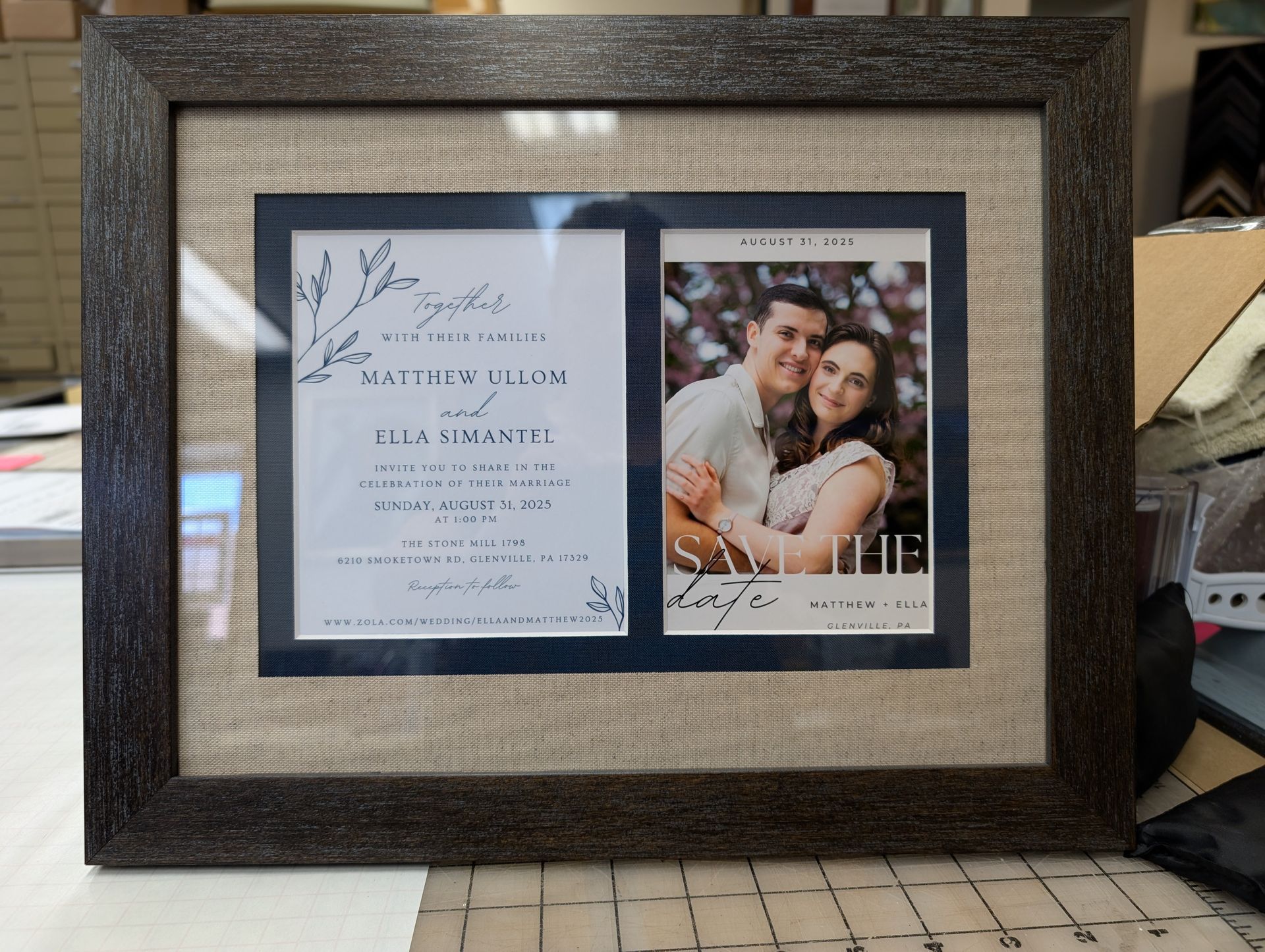 Framed wedding photo and invitation display with gray mat and floral accents.