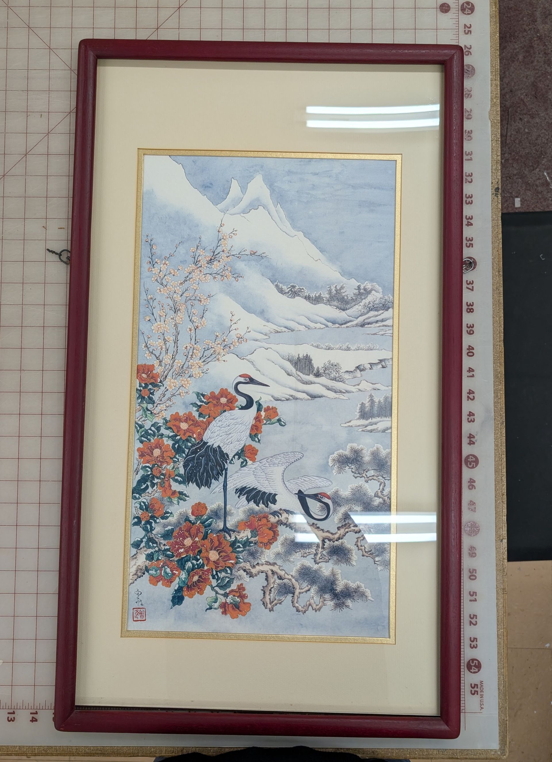 Framed artwork of snowy mountains with red flowers and birds in a burgundy frame.