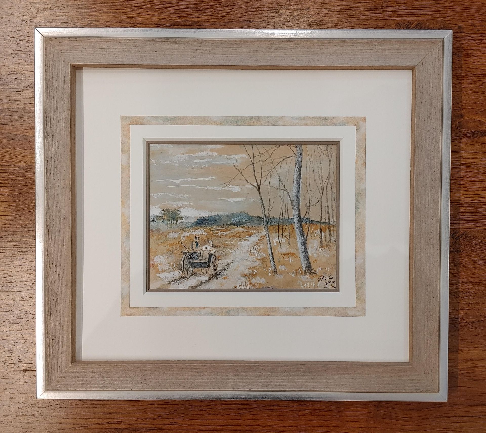 Framed landscape painting with muted beige and gray tones, centered in a layered cream frame on a wooden surface.