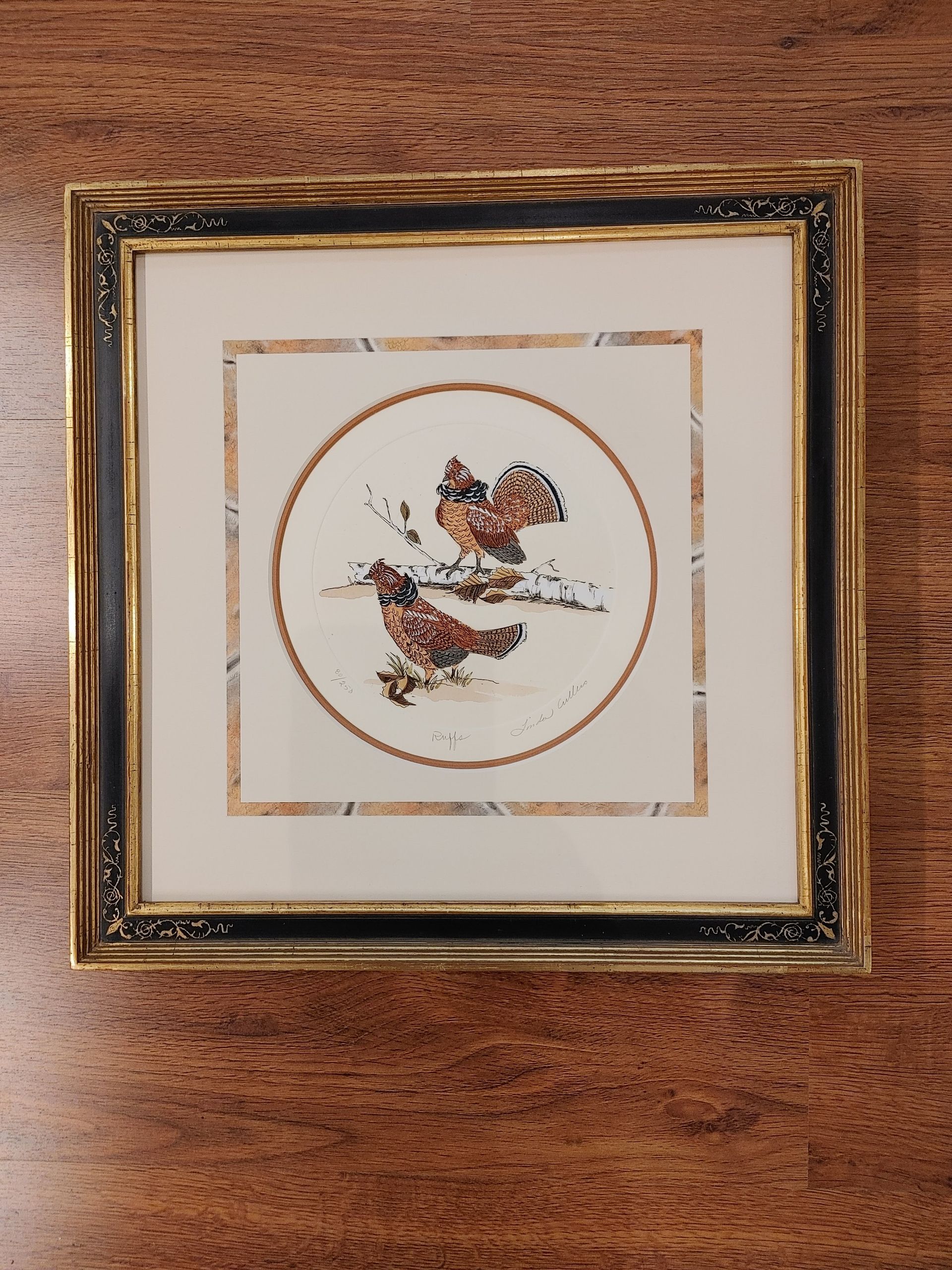 Framed botanical print with a small bird in a gold-trimmed frame on a wooden wall.