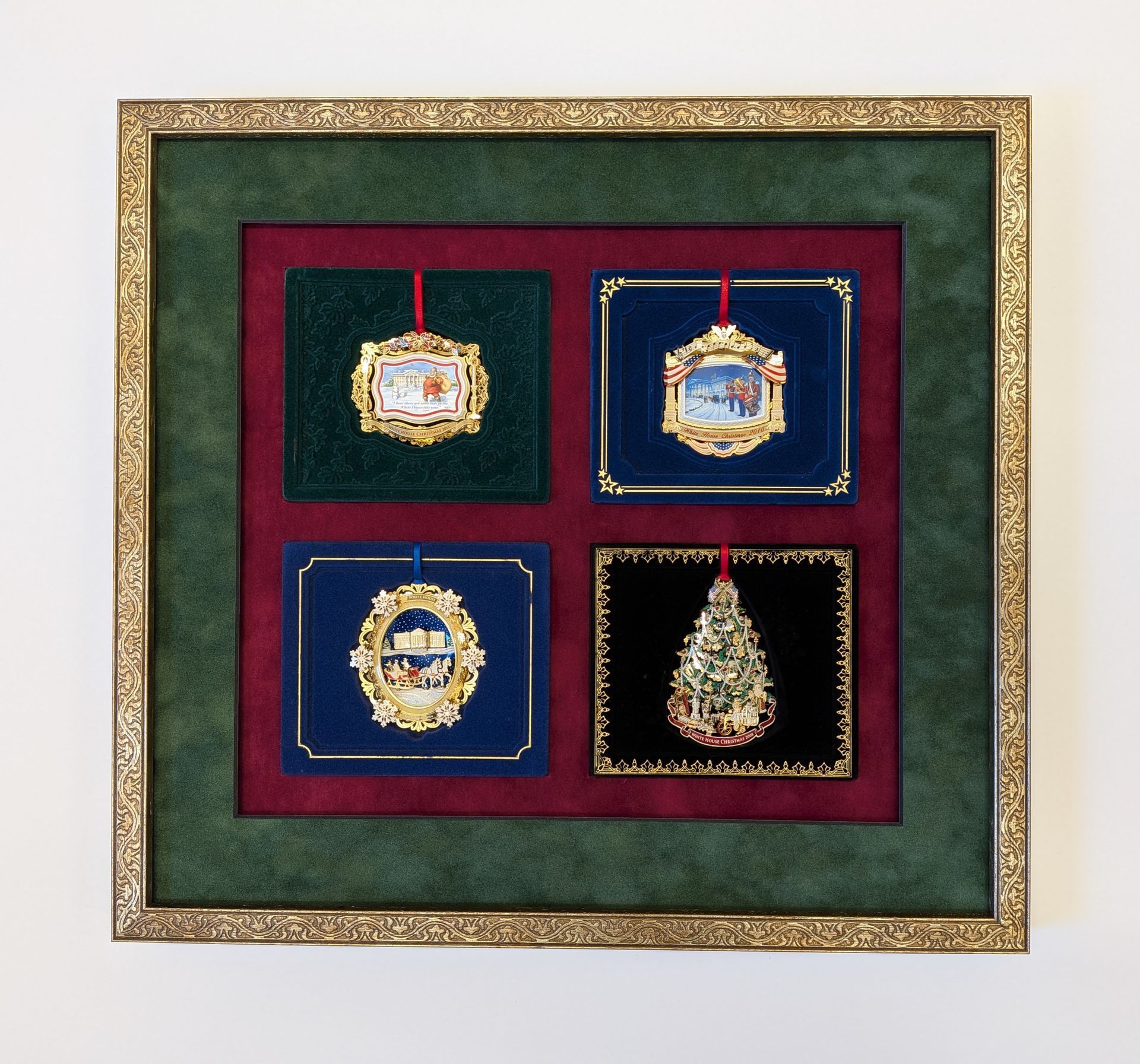 Framed display of four ornate medals on velvet backgrounds in gold, green, red, and blue.