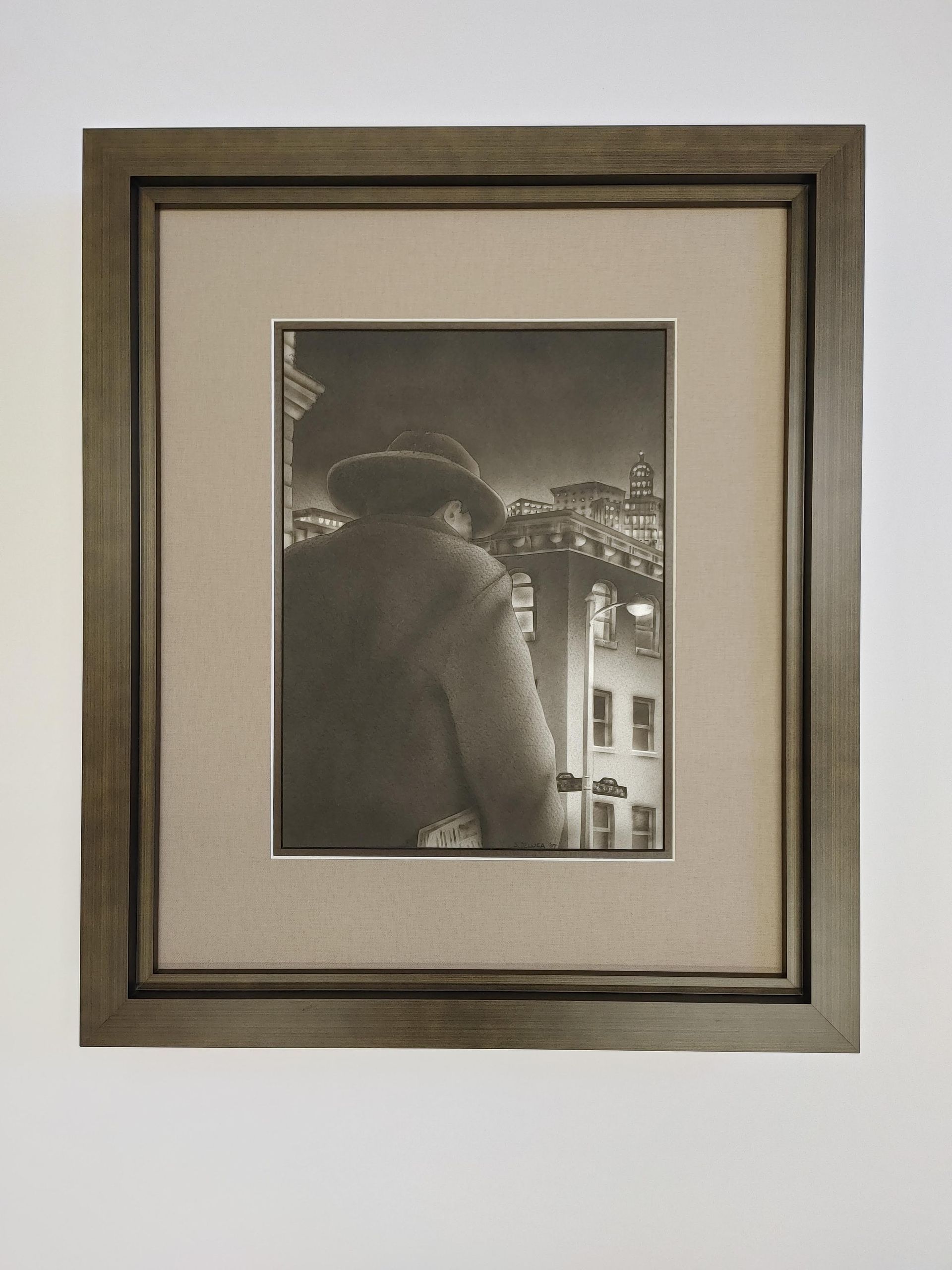 Framed black-and-white photo of a person in a coat and hat overlooking a lit city at night.