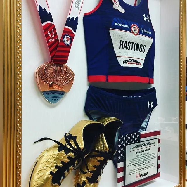 Swimming memorabilia: medals, racing suit, jersey, shoes, and a plaque mounted on a wall.