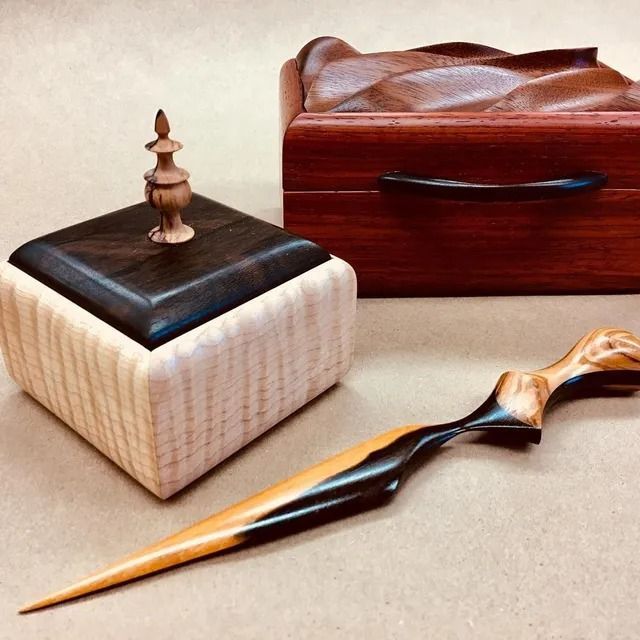 A small light-wood box with a dark lid and finial, a carved reddish box, and a two-toned wooden letter opener.