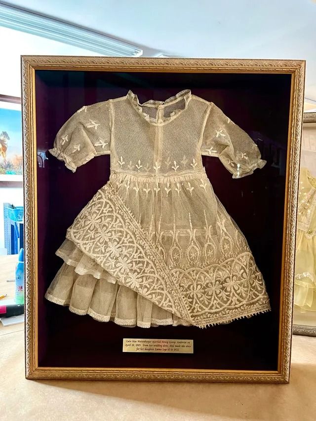 Gold dress displayed in a framed shadow box with a plaque beneath it.