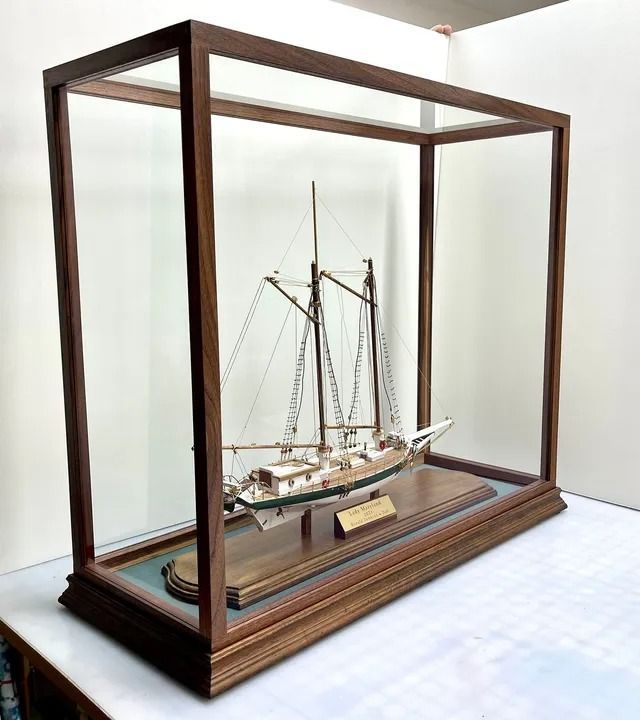 A model ship inside a wooden display case with a glass top, sitting on a table.