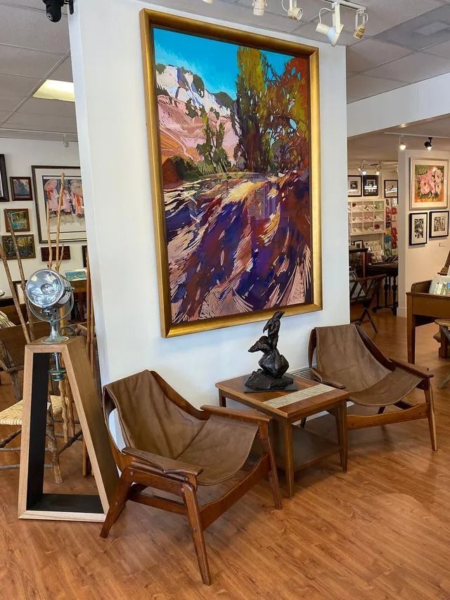 Art gallery seating area with two wooden chairs, a small table, and a large colorful landscape painting on display