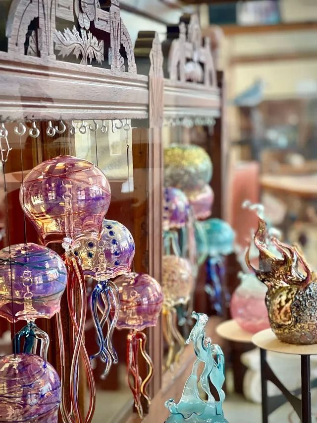 Colorful glass art figurines displayed on shelves and a small table in a shop.