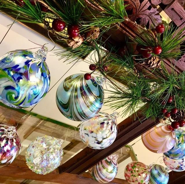 A collection of decorative glass orbs hanging from a wooden shelf with artificial pine needles and red berries.
