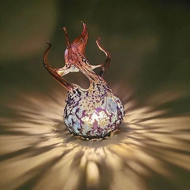A decorative glass lamp with a textured purple and white base, casting intricate light patterns onto a surface.