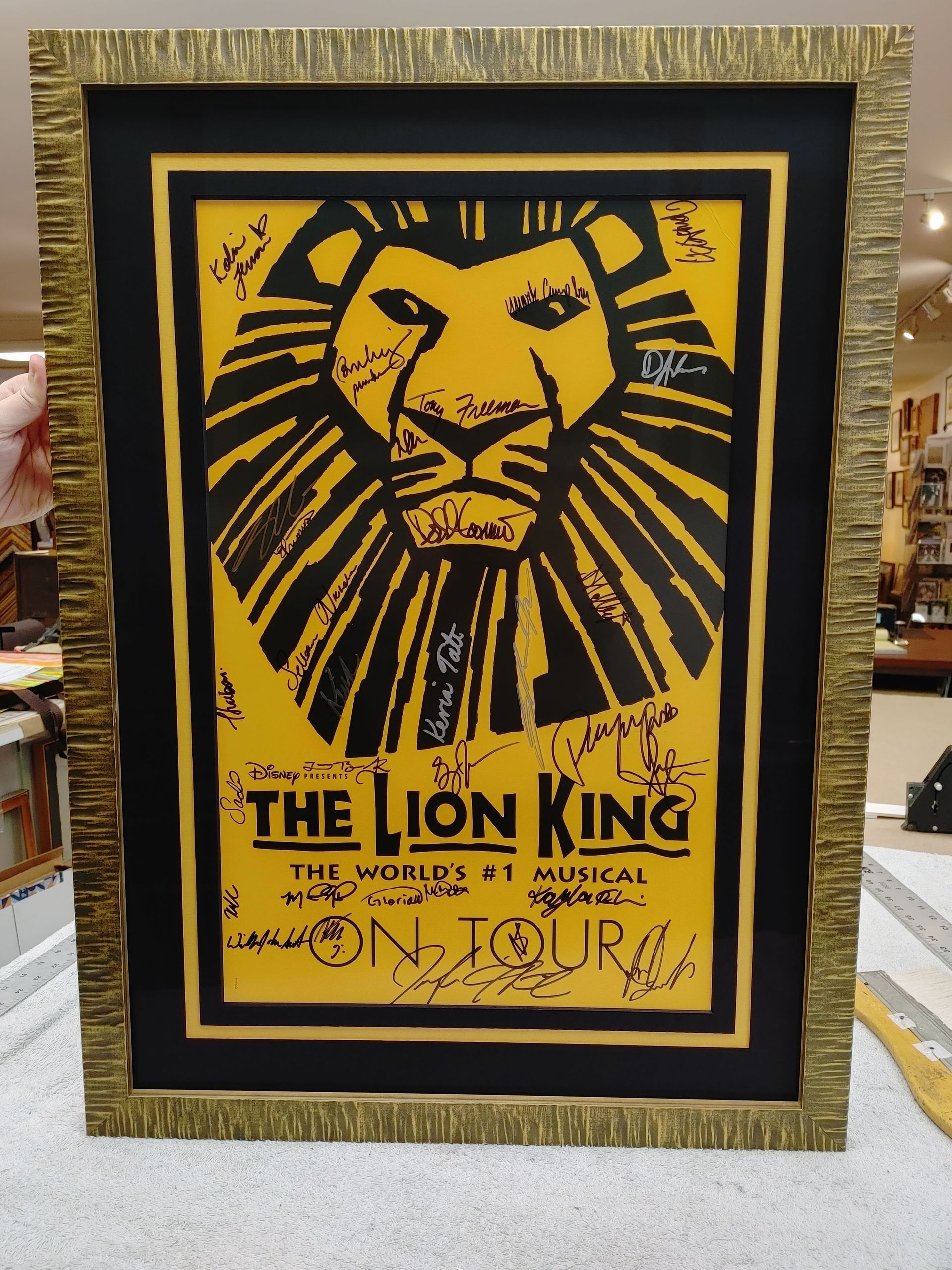 Framed yellow and black Lion King poster on display with ornate gold border.