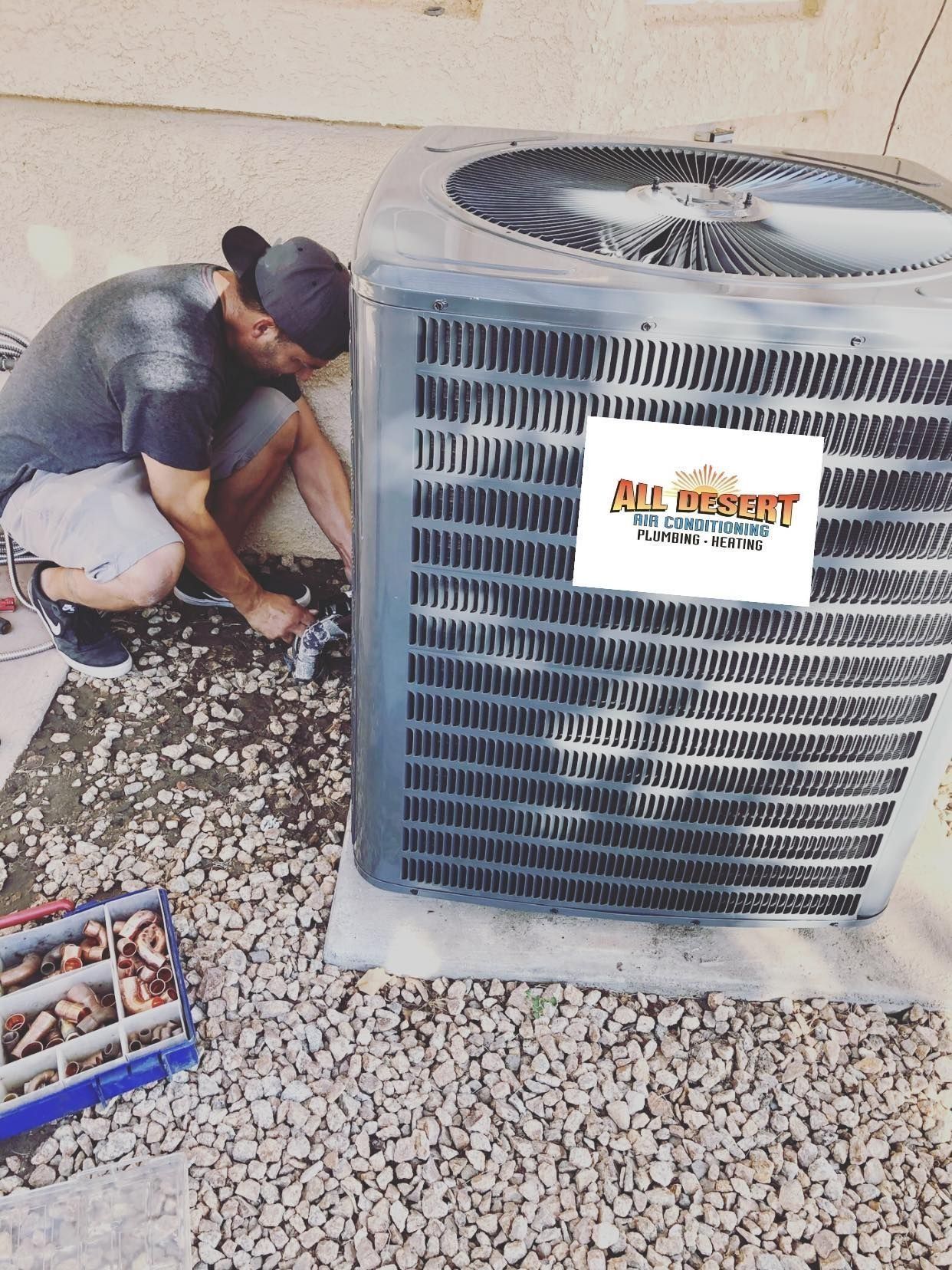 Man working on an air conditioning unit outside, on a bed of rocks, with tools nearby.