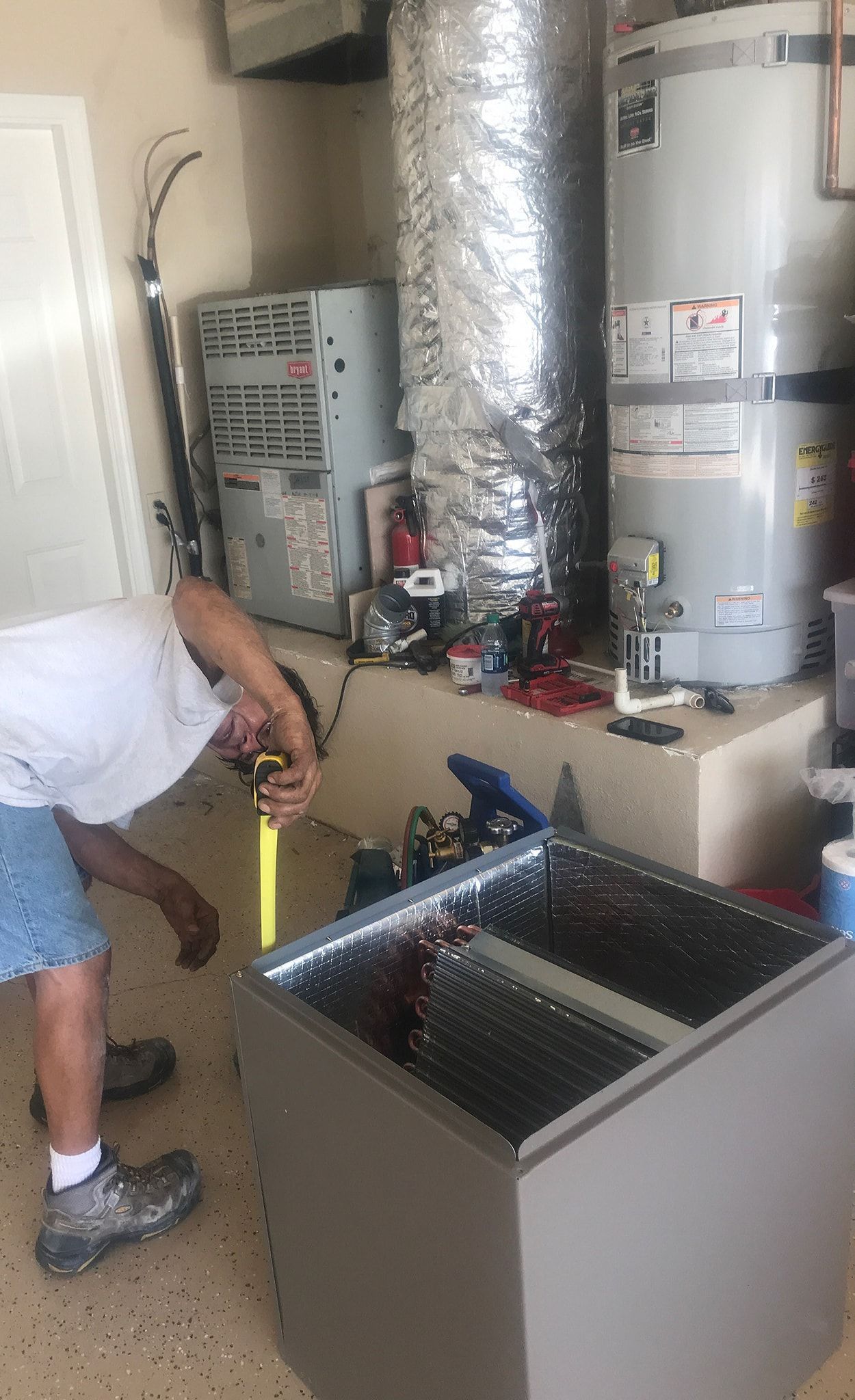 Man in garage repairing HVAC unit, next to water heater and ductwork.