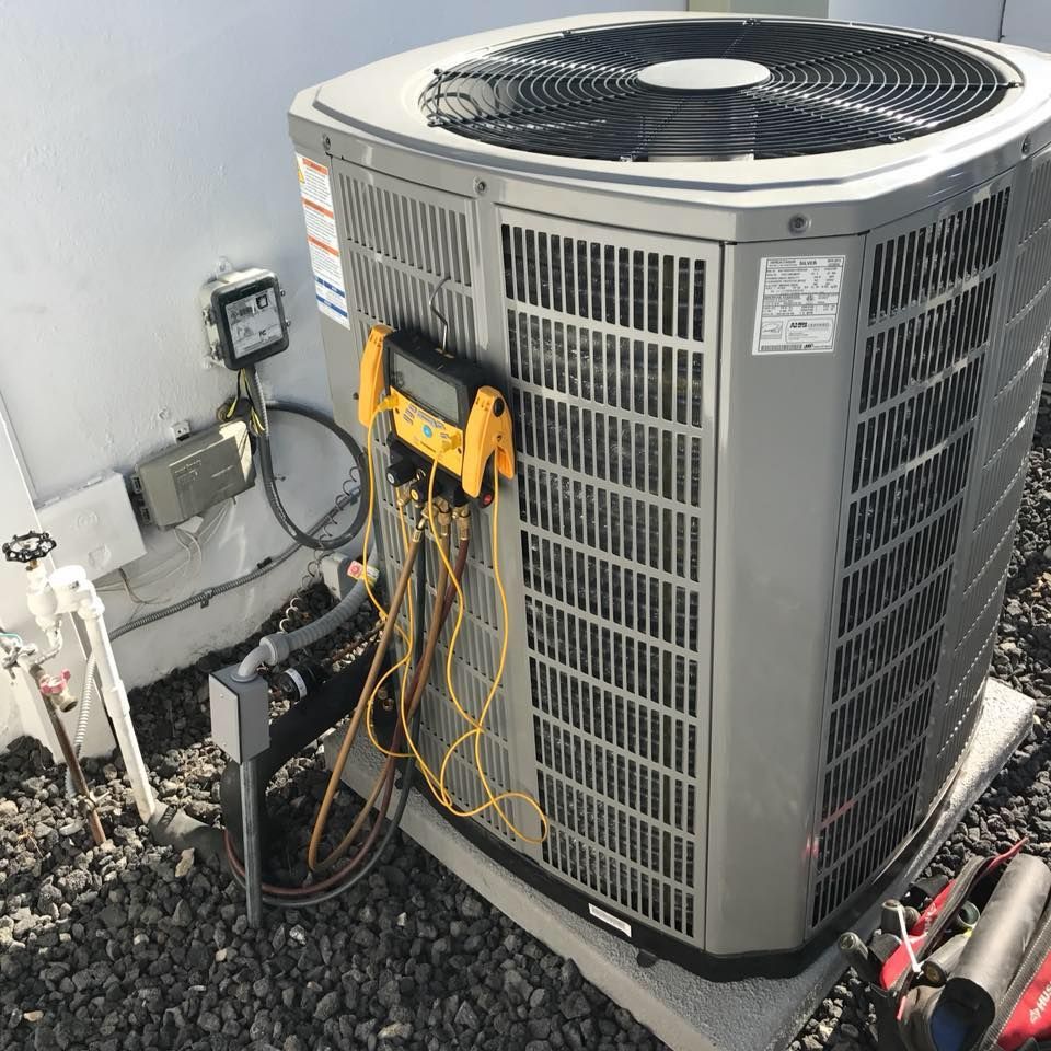 AC unit being serviced on a rooftop; yellow gauges and black hoses attached.