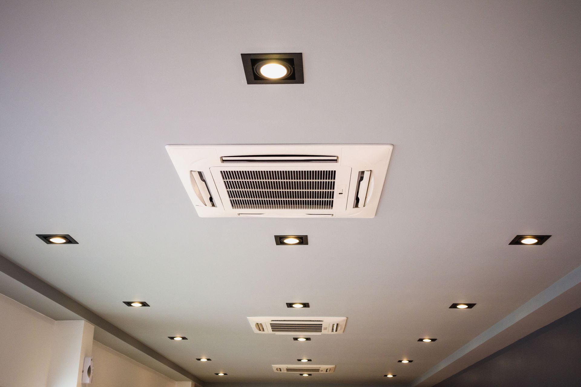 White ceiling with recessed lights and two ceiling-mounted air conditioning units.