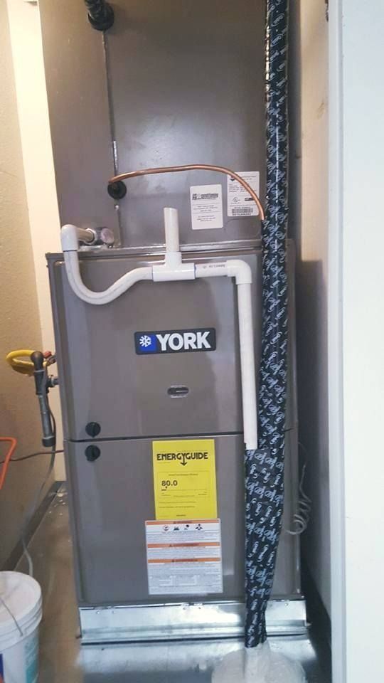 A York furnace in a utility closet with white PVC pipe and black insulated tubing.