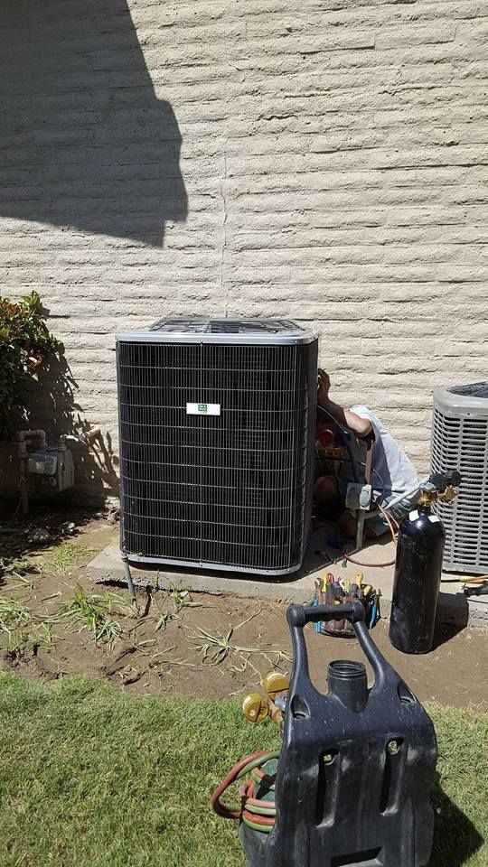 AC repair: Technician working on outdoor unit near a wall. Tools and gas cylinders are present.