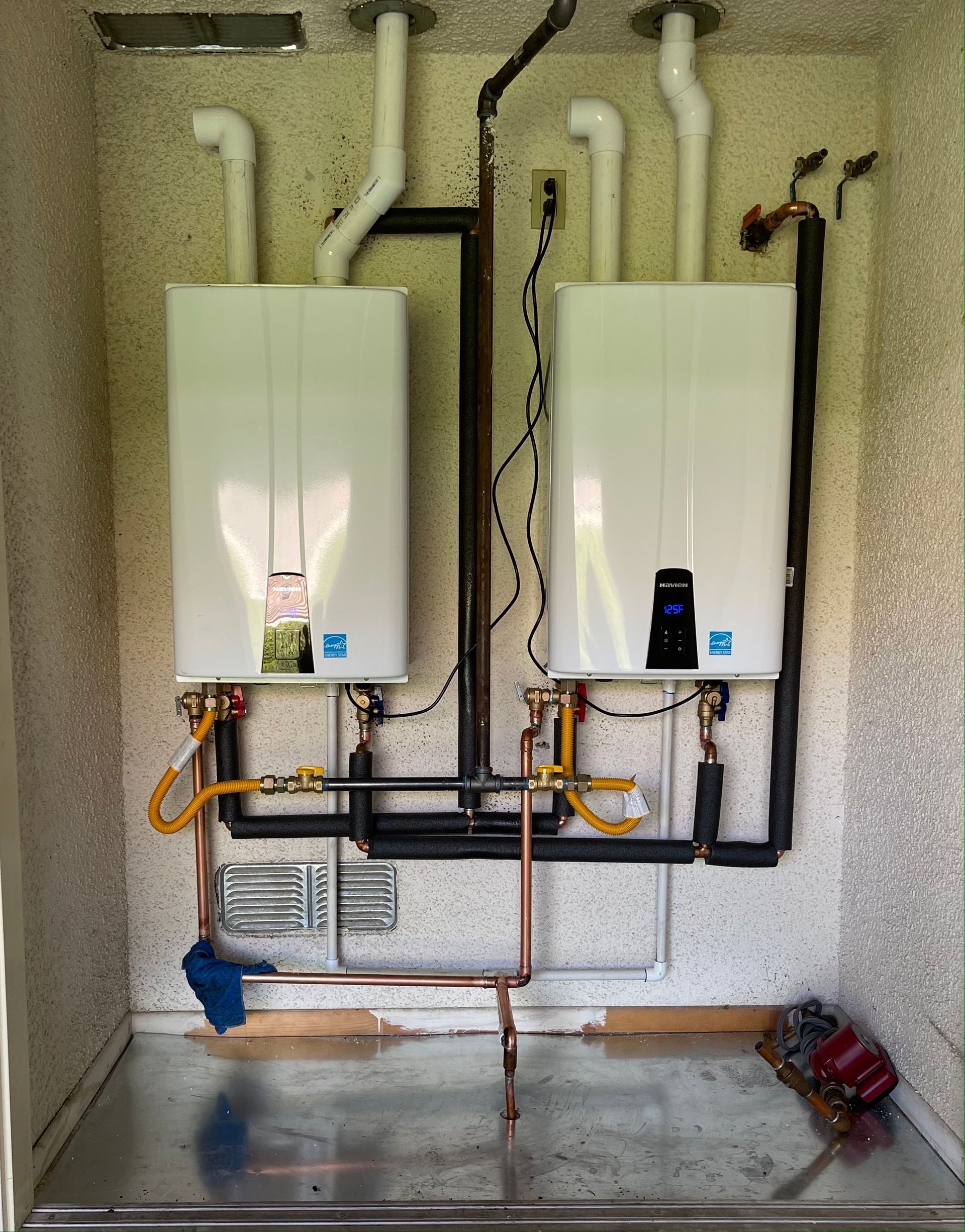 Two white water heaters installed indoors, with pipes and vent systems.