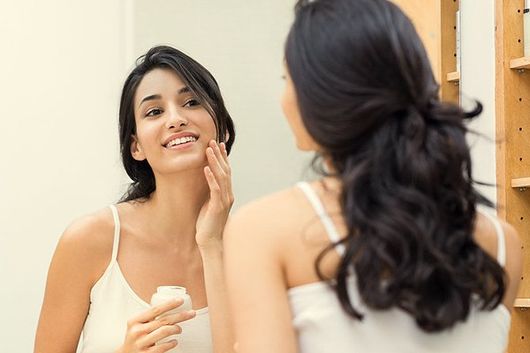 Young woman applying moisturizer on her face