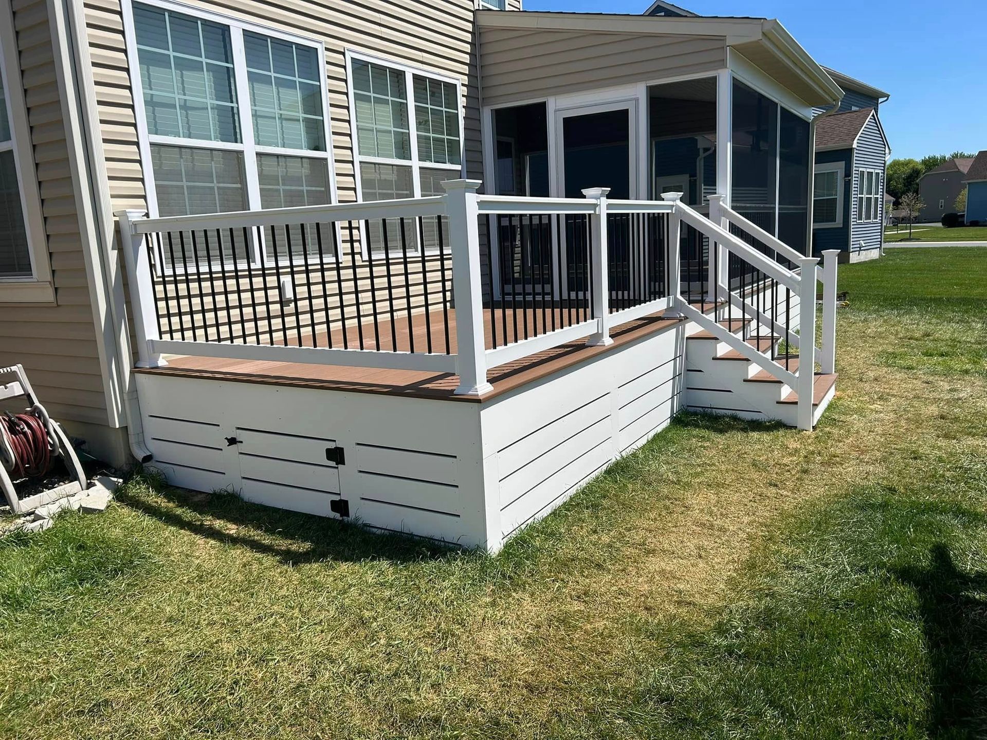 White deck with brown decking, attached to a house with a screen porch, set in a grassy yard.