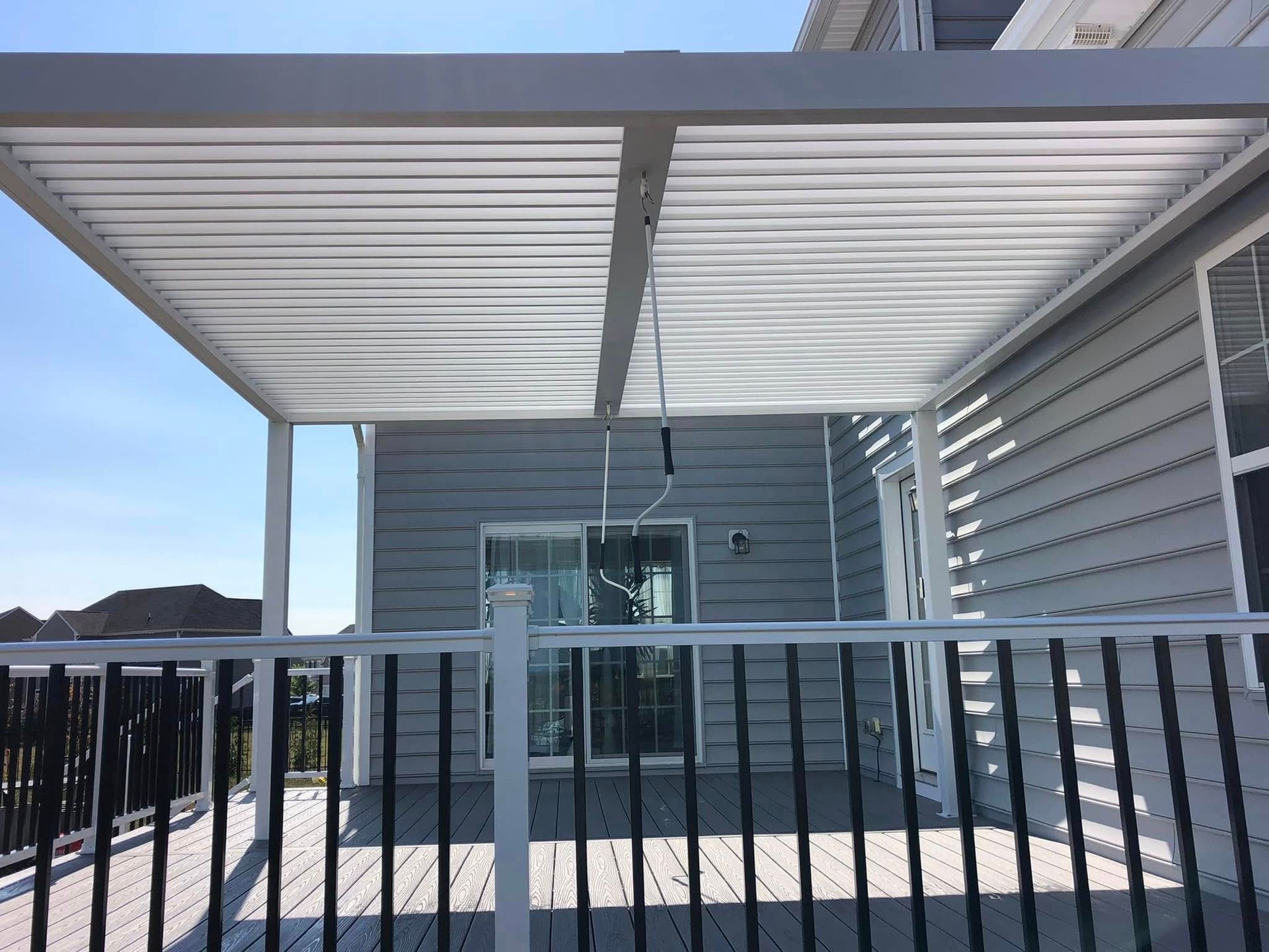 White patio cover over a wooden deck with black railing, attached to a house with gray siding.