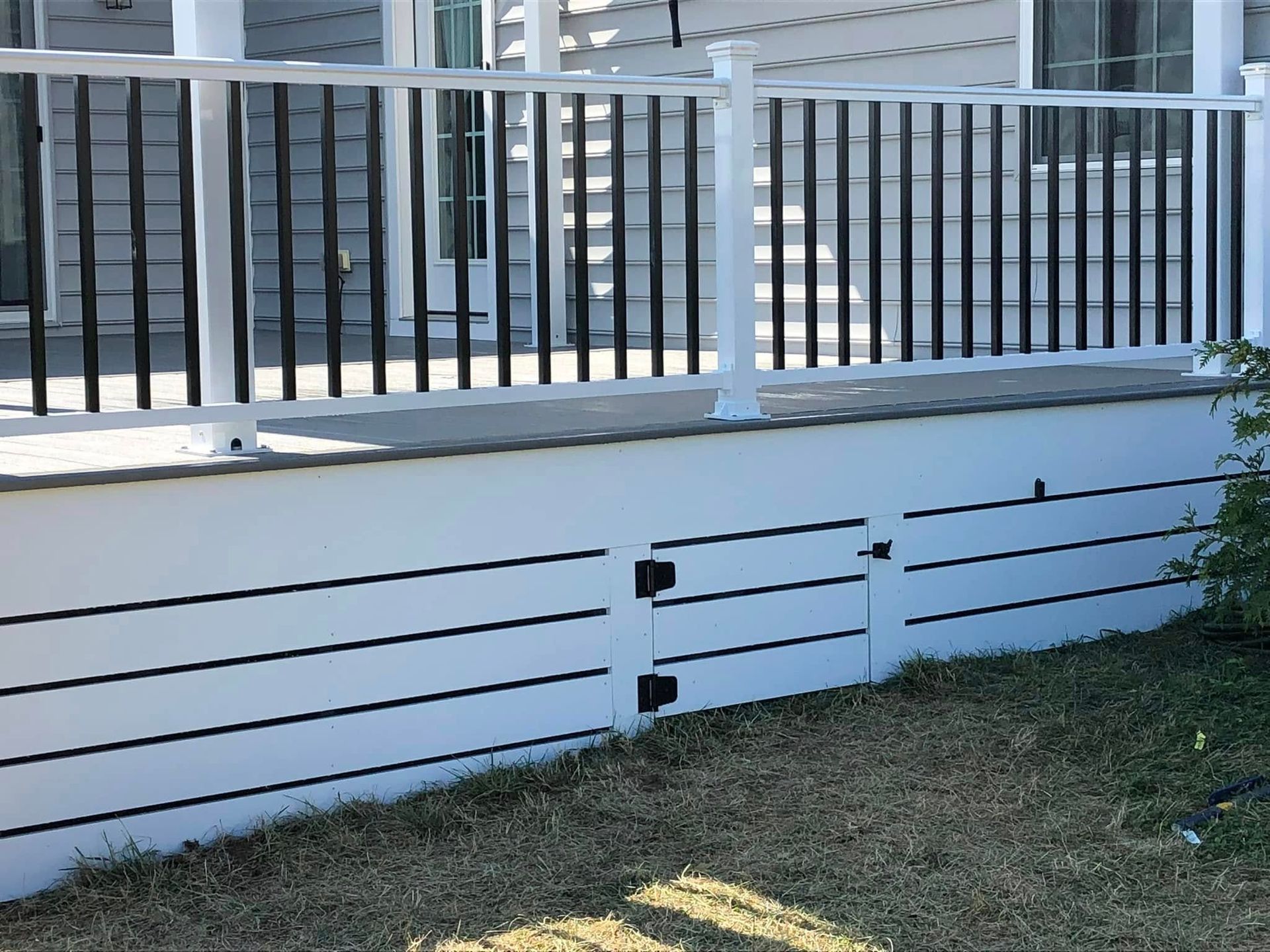 White deck with black railings and skirting, with a small door, sitting on a grassy yard.