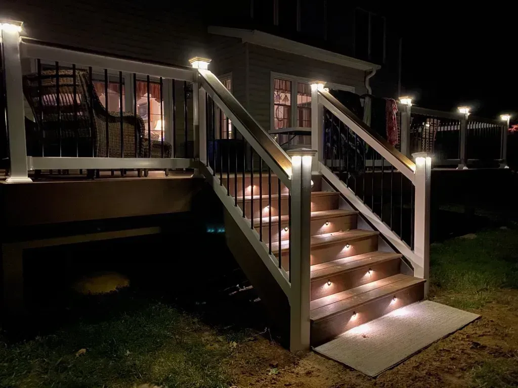 Lit deck steps at night with built-in lights and railing lights, leading to a dark deck.
