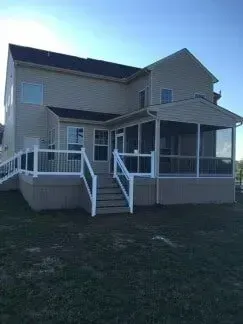 Two-story house with a screened porch and deck. White railing, tan siding, and dark roof on a grassy lawn.