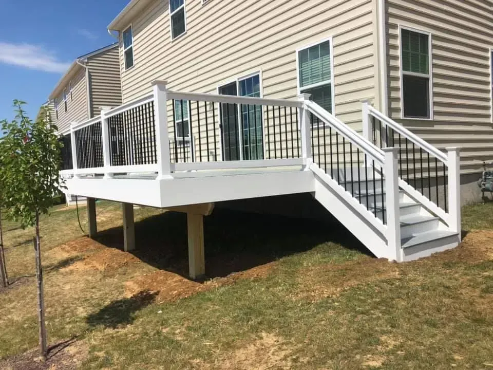 White deck with black railing and steps attached to a light-colored house, on a grassy hill.