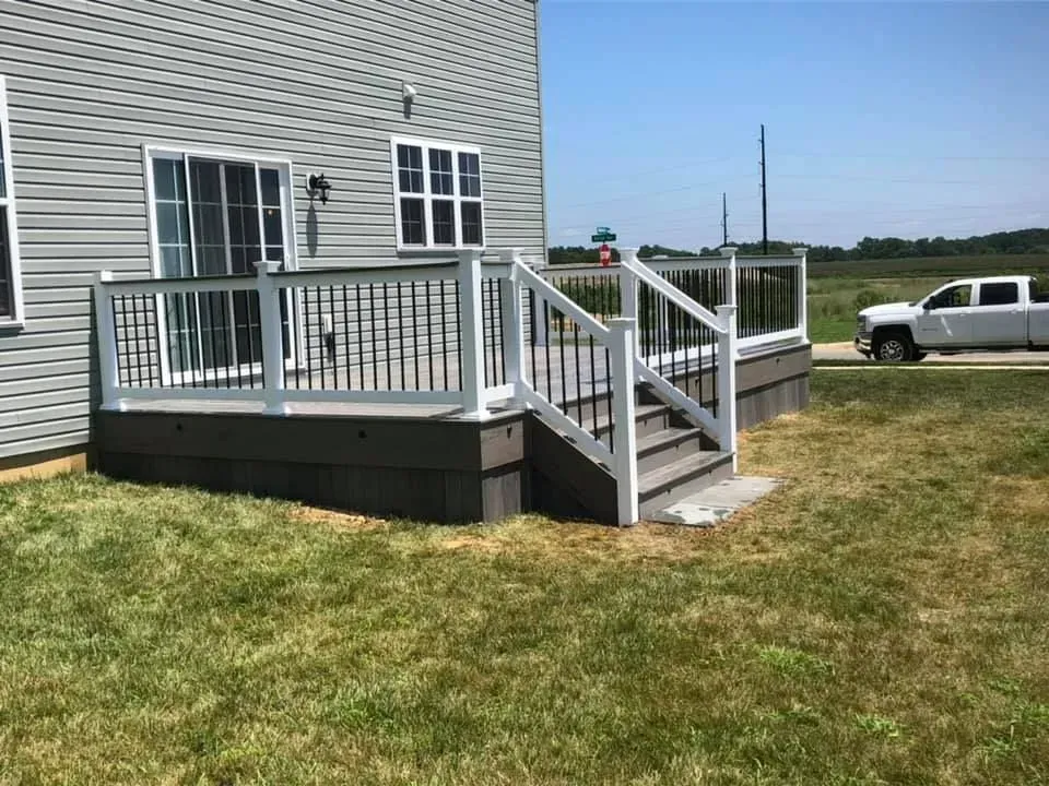 A gray deck with white railings and black spindles, attached to a gray house, set on grass.