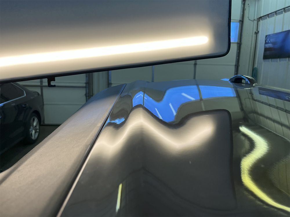 Car roof with large dents being inspected under a bright light in a repair shop - after.