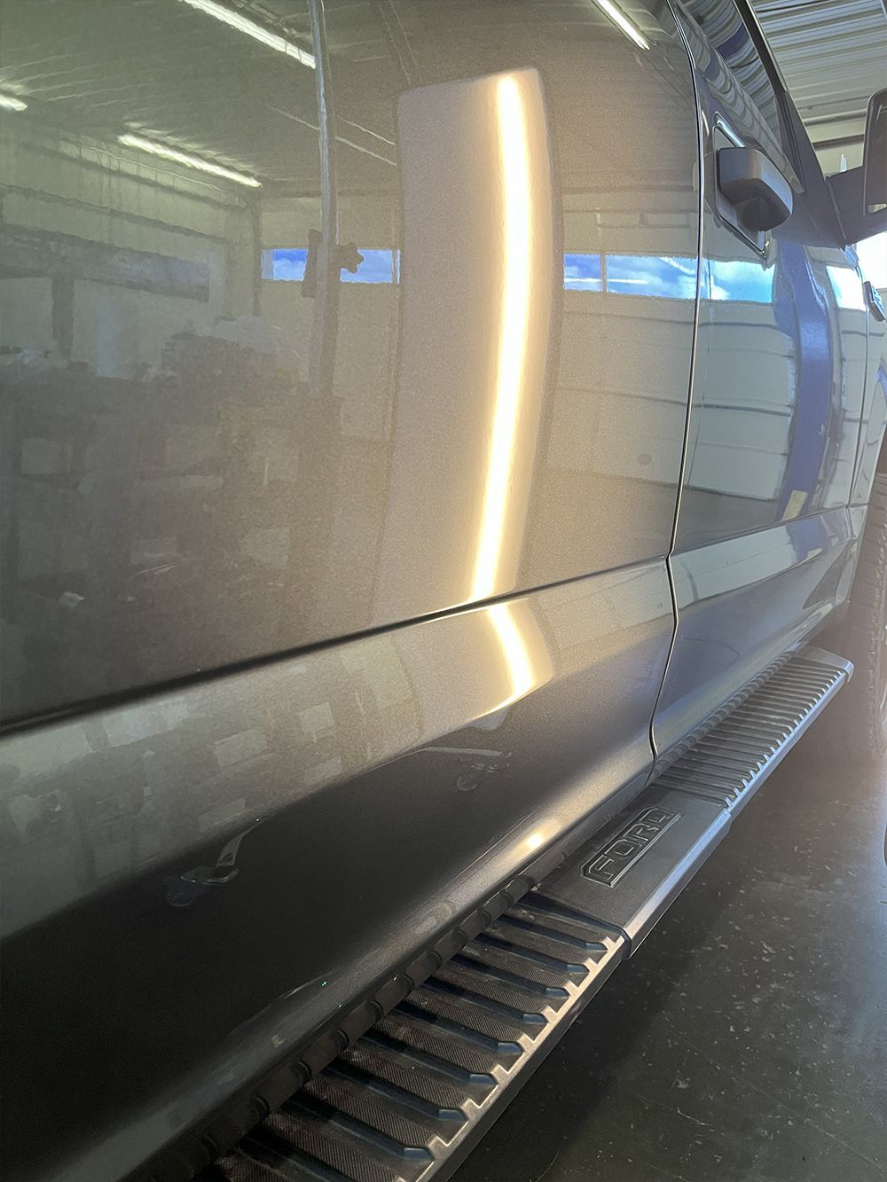 Gray truck door with a large dent, reflecting overhead lights - after.