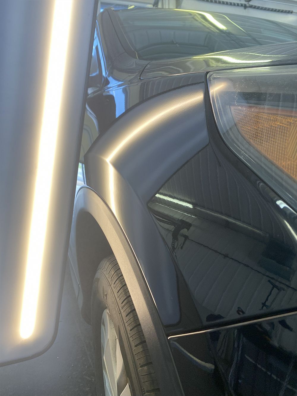 Black car with dent on rear quarter panel being assessed with a light for repair - after.