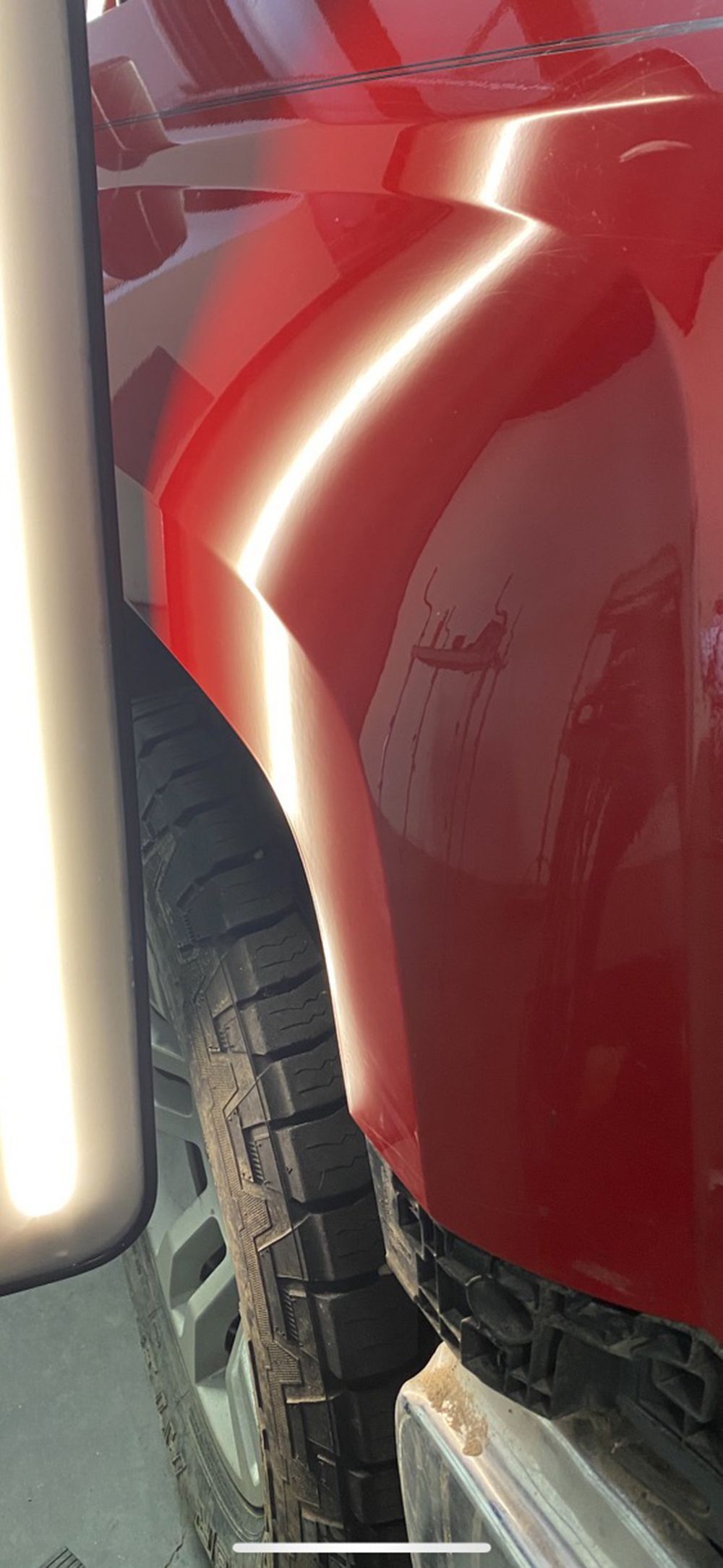 Red car's dented side panel near a tire, with reflection highlighting the damage - after.