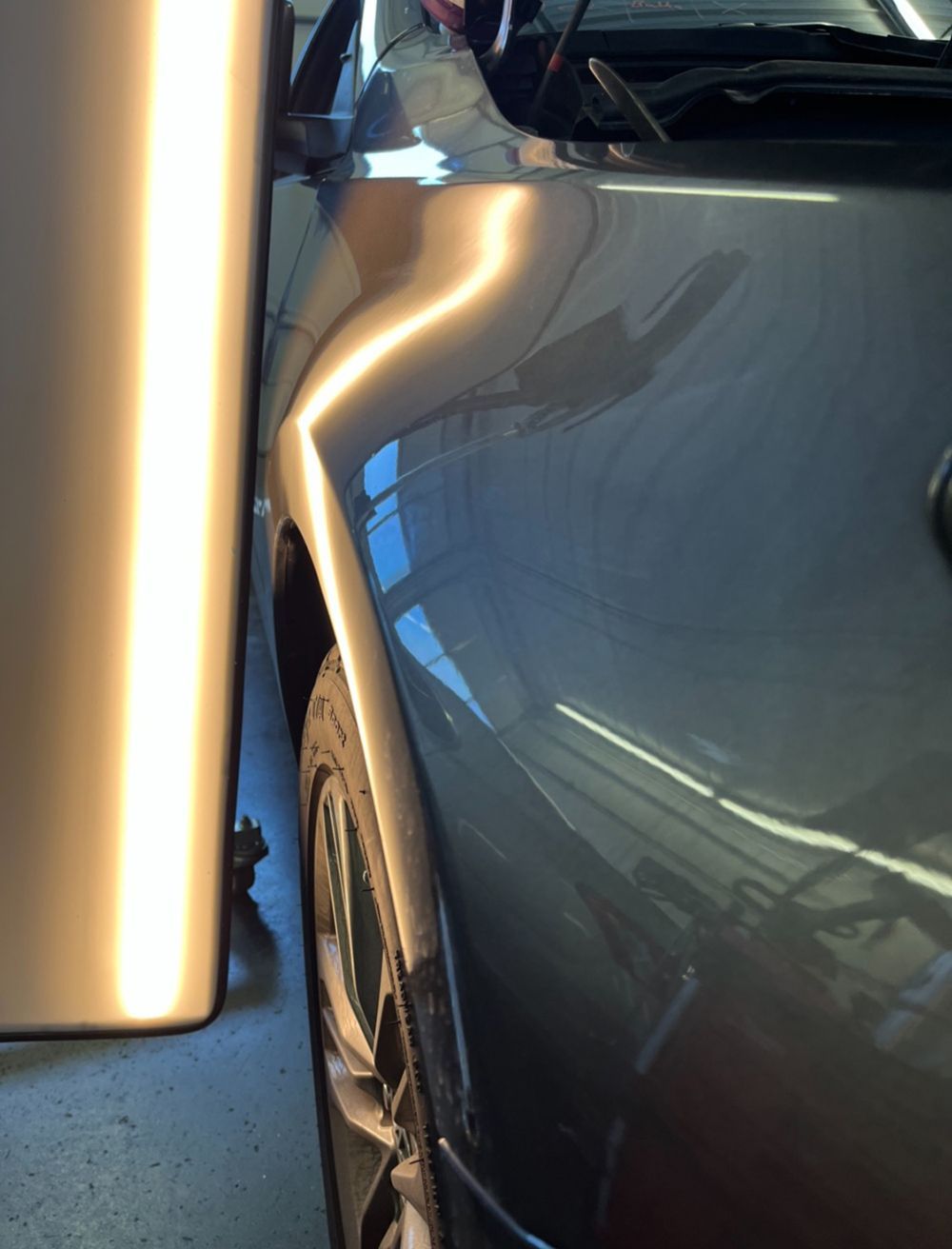 Gray car fender with a dent, illuminated by a light for repair - after.