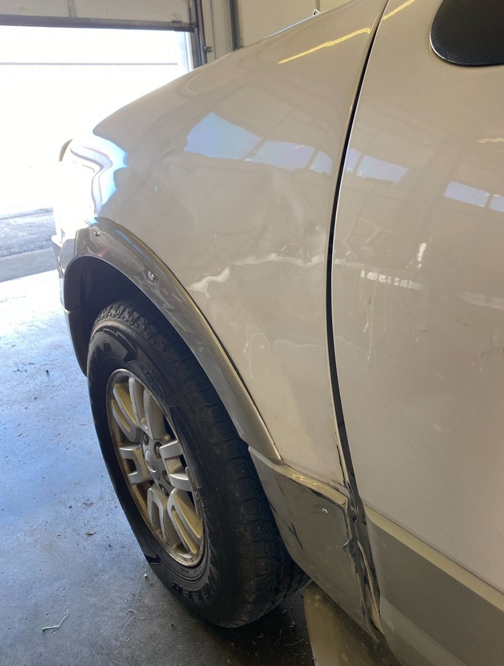 Damaged white car fender with dent and scraped paint - after.