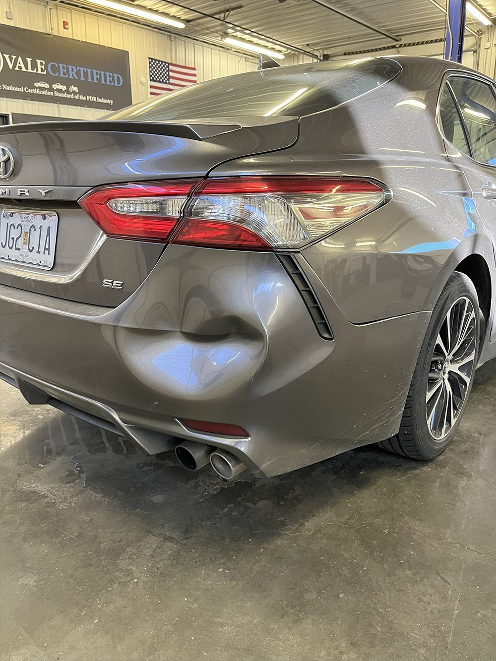 Brown Toyota Camry with a large dent in the rear panel, inside a garage - before.