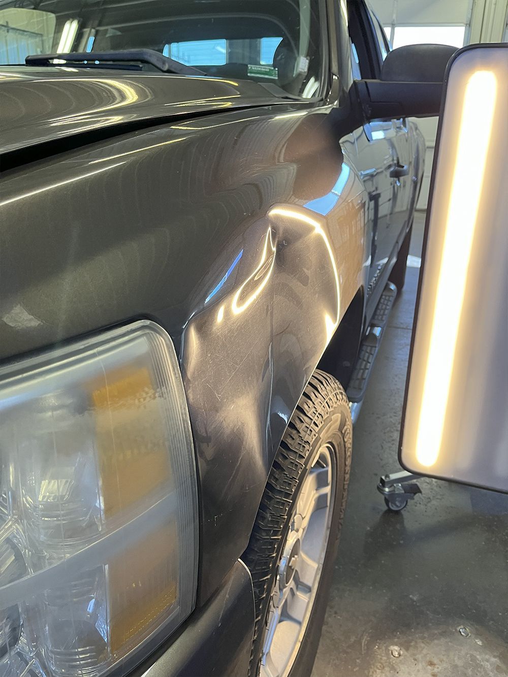 Gray truck with a large dent in the front fender, viewed indoors under a bright light - before.