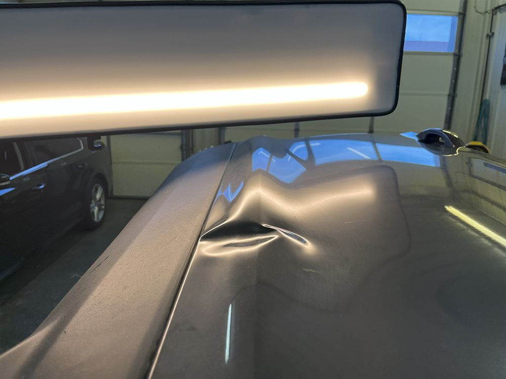 Gray car roof with a prominent dent, being examined with a reflective light for repair - before.