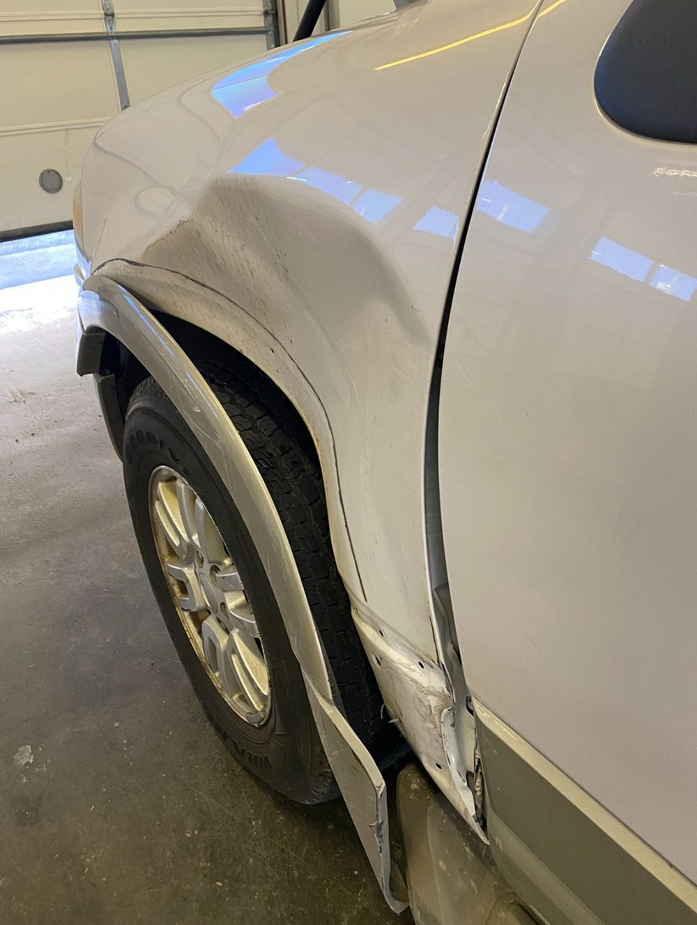 White car with significant dent and damage to the front quarter panel above the tire - before.