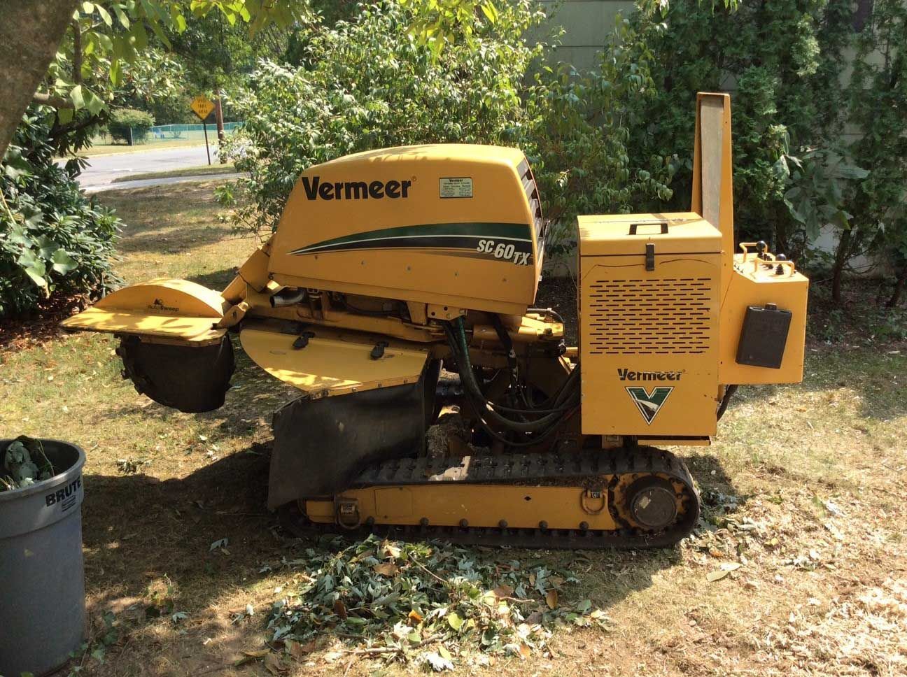 Yellow Vermeer stump grinder on tracks, in a yard, grinding wood.