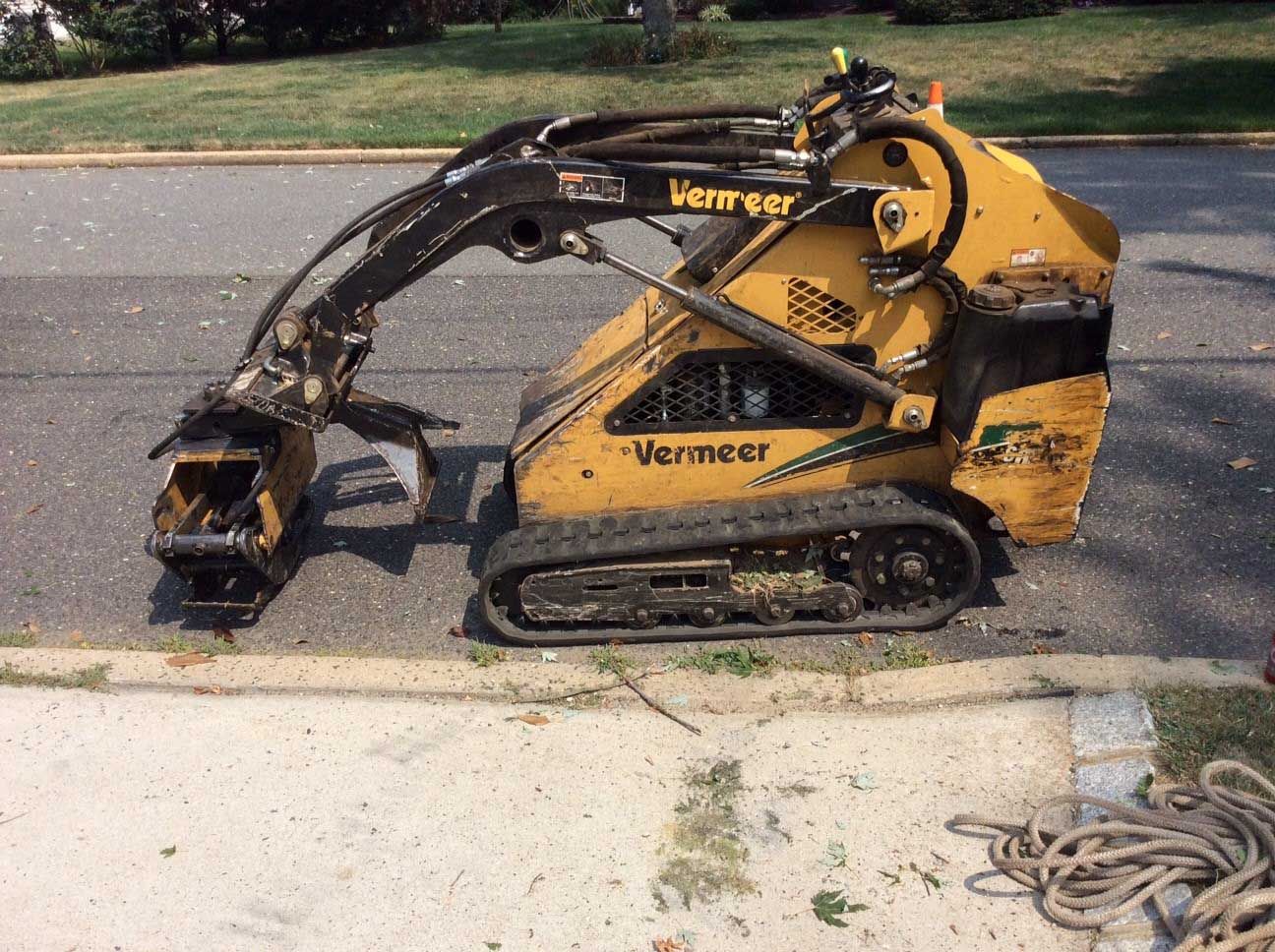 Yellow Vermeer mini skid steer with a grapple attachment on pavement.