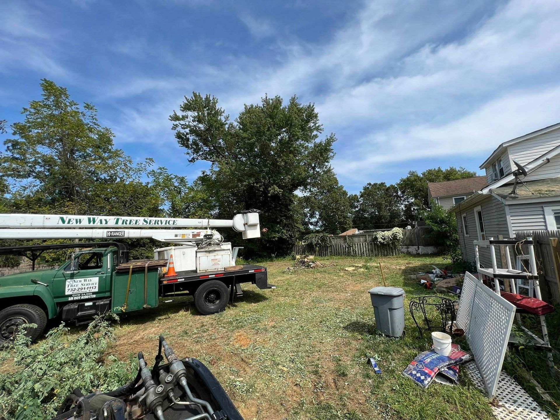 Green tree service truck with boom near a tree; backyard with debris.