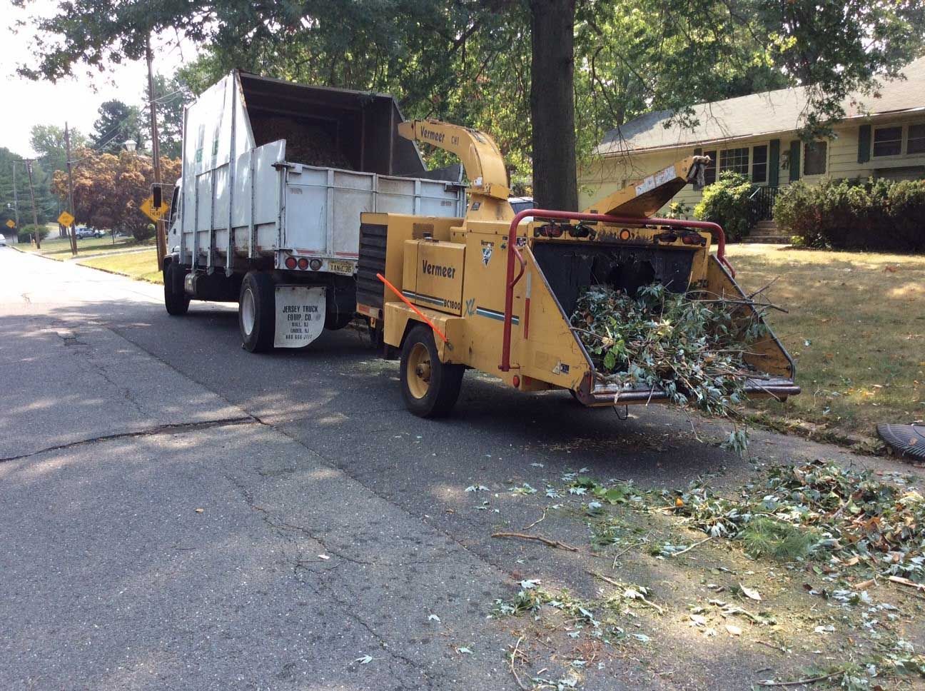 Truck with wood chipper loading yard waste on street.