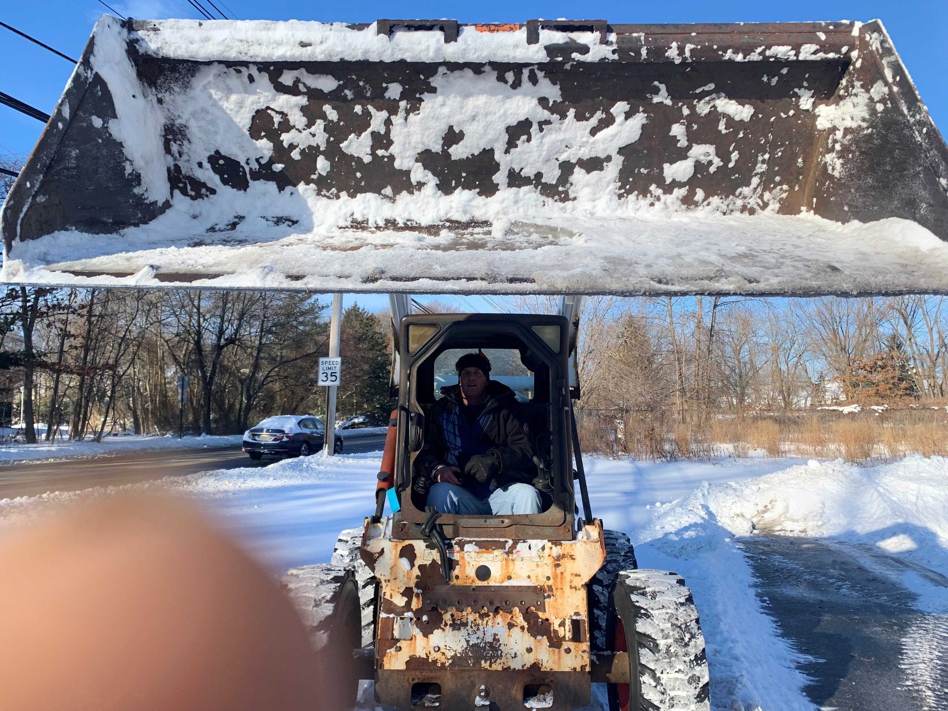 Man operating a snowplow on a snowy road. Bucket of the plow is full of snow.