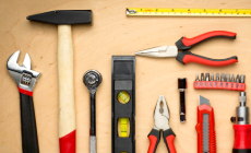Assortment of hand tools, including a hammer, wrench, pliers, screwdriver, utility knife, and level, on a beige surface.